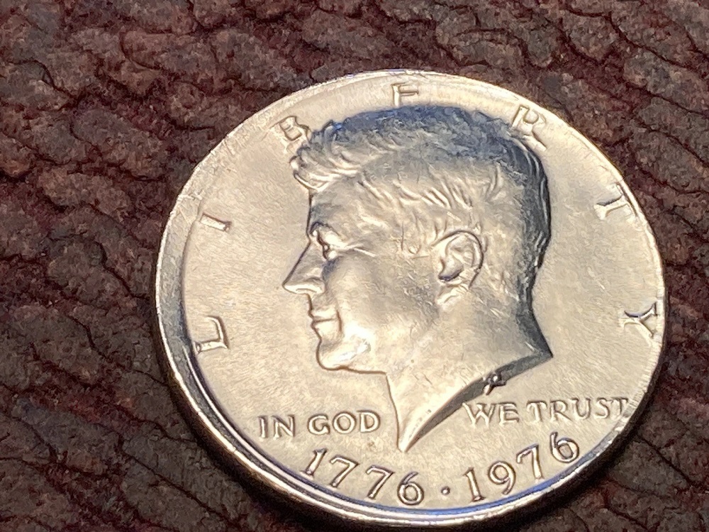 1976 Kennedy half dollar off-center strike showing design shifted to one side with blank crescent area and dual date visible